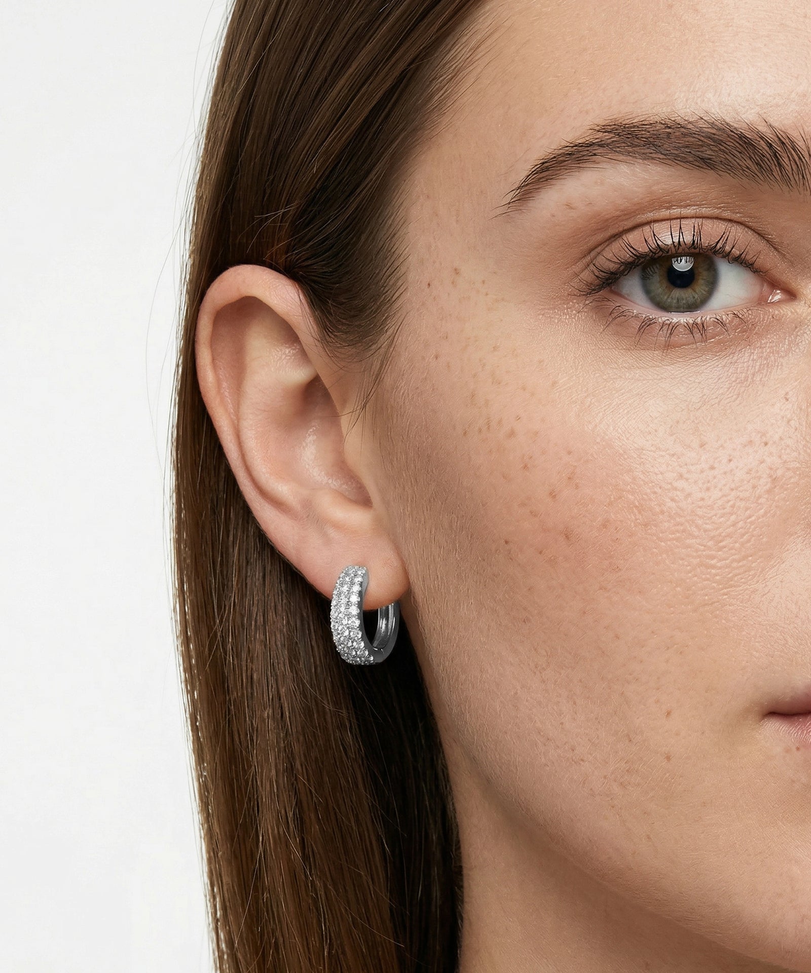 Close-up of a woman wearing silver hoop earrings with a plain background