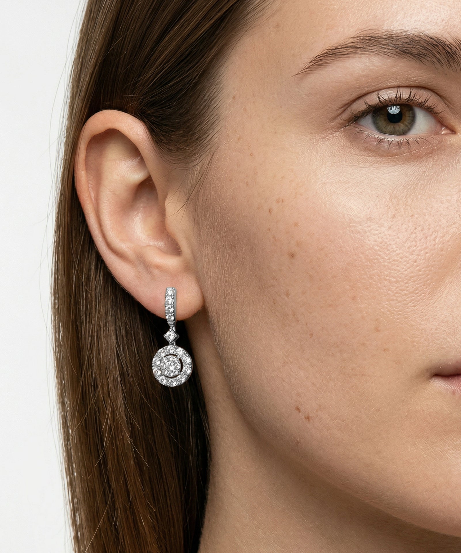 Close-up of a woman wearing diamond earrings with a neutral background