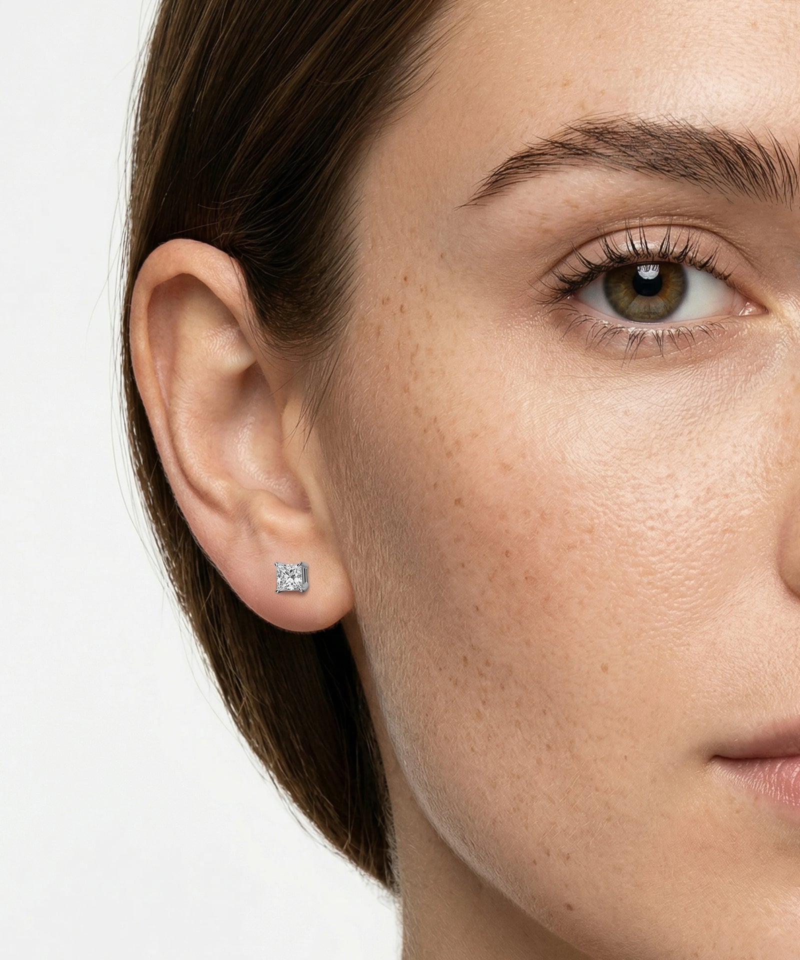 Close-up of a woman wearing a diamond stud earring on a plain background