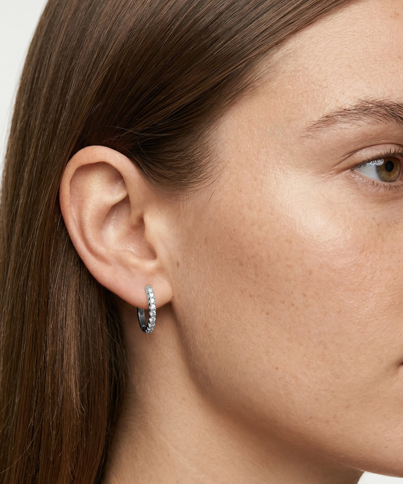 Close-up of a person wearing a silver hoop earring with small stones.