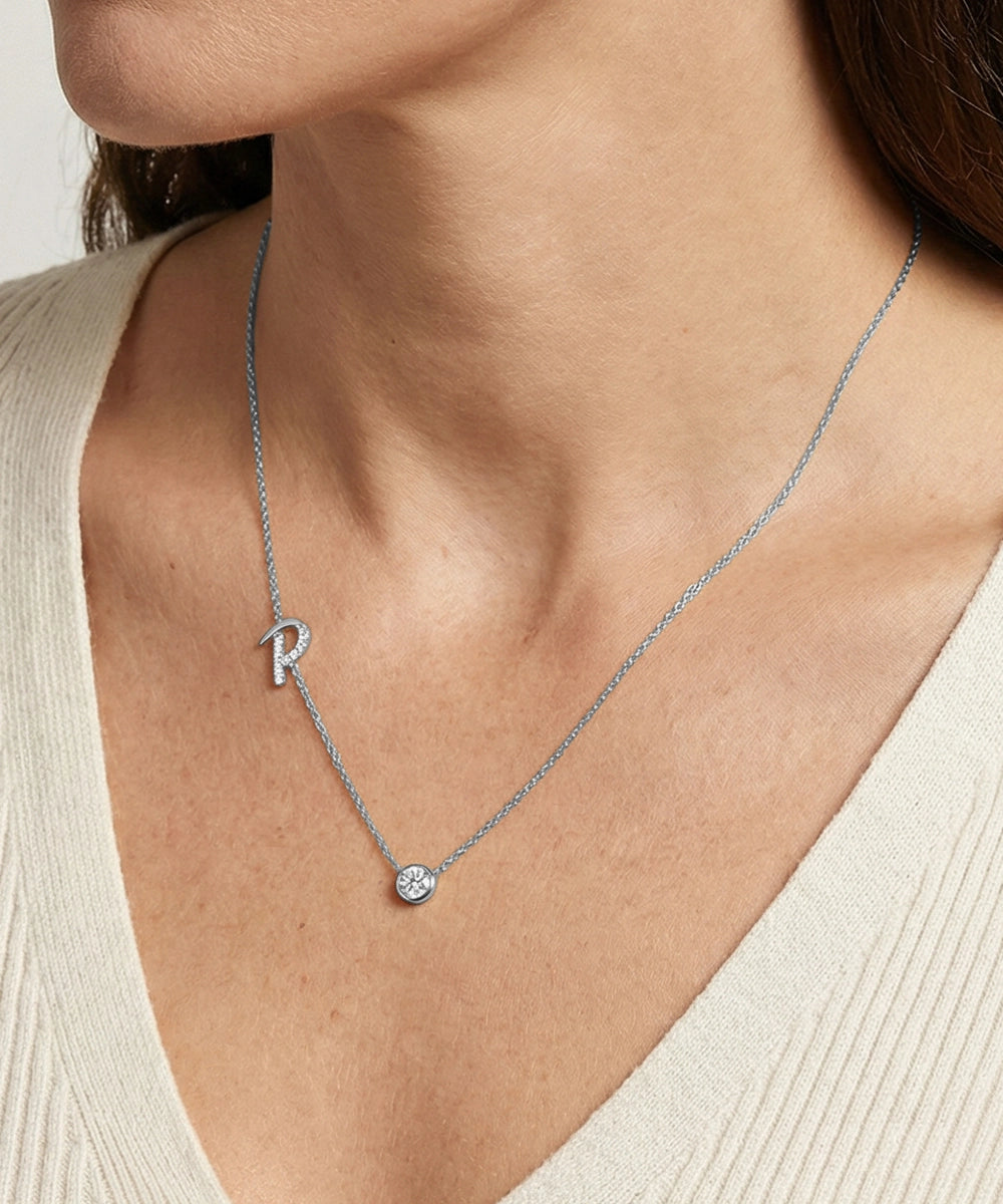 Necklace with a letter 'R' pendant on a person wearing a beige top.
