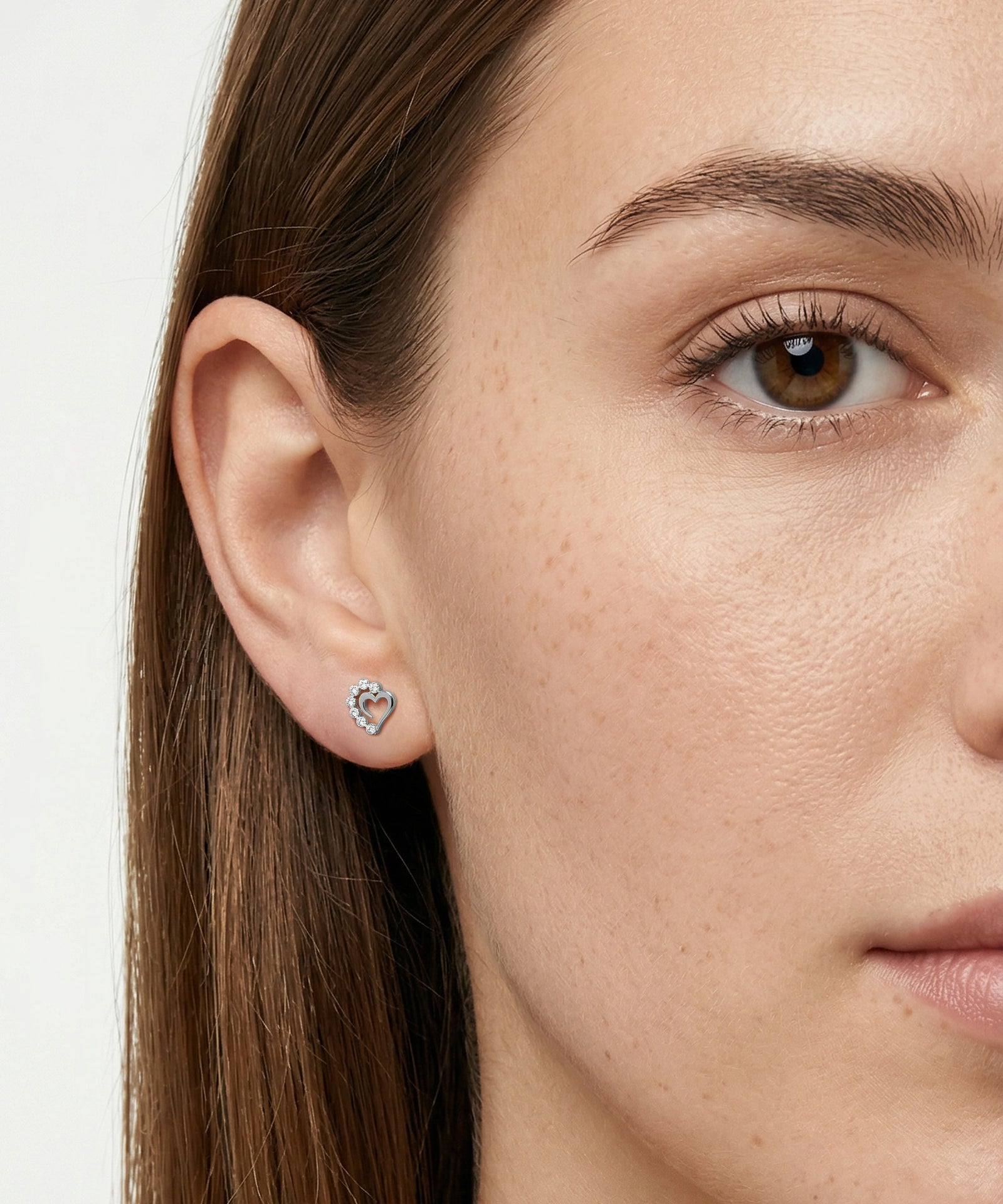 Close-up of a woman wearing a heart-shaped earring on a plain background