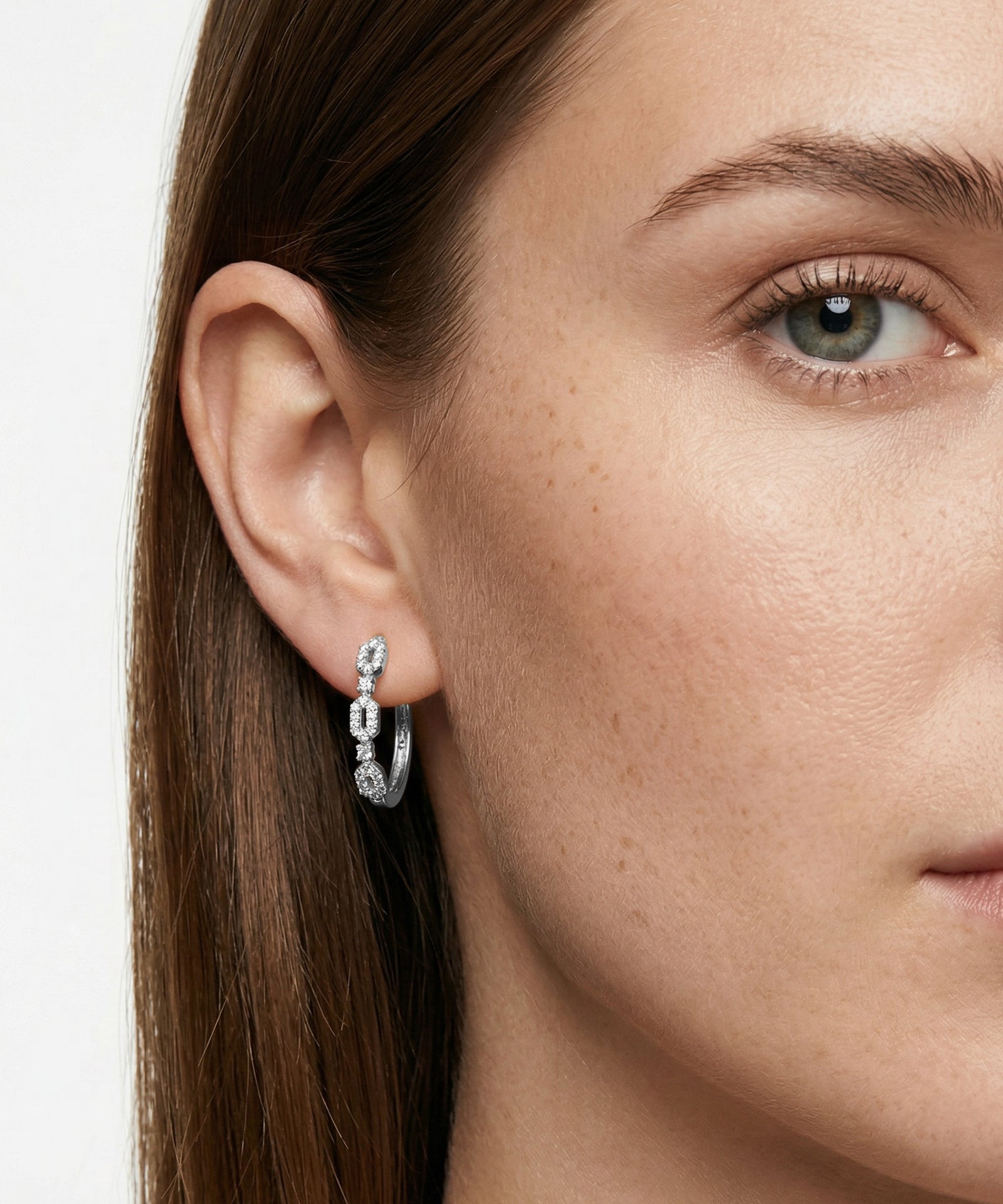 Close-up of a woman wearing a silver hoop earring with clear stones.