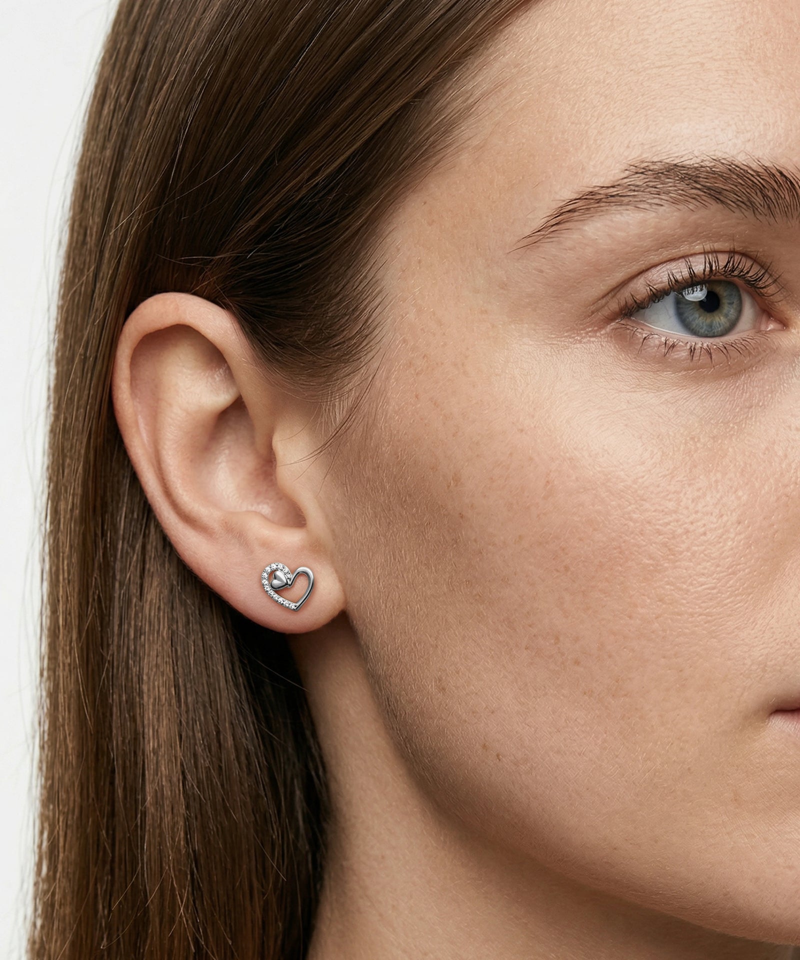 Close-up of a woman wearing a heart-shaped earring on a plain background