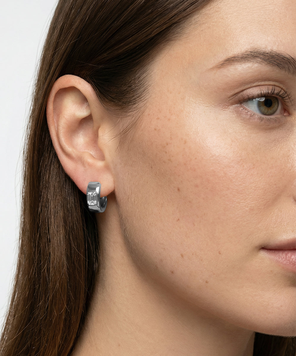 Close-up of a woman wearing a silver hoop earring with a plain background