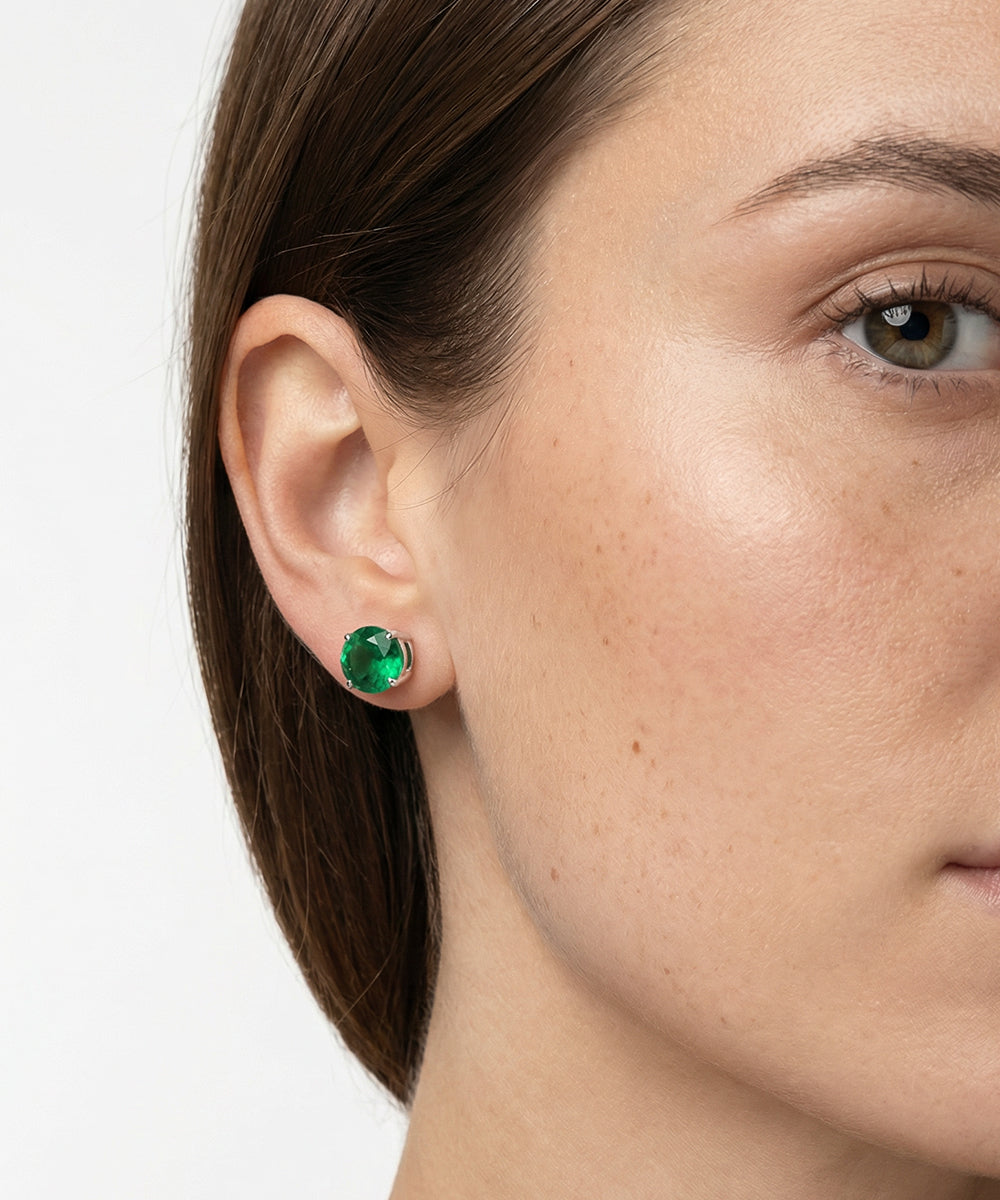 Close-up of a woman wearing green gemstone earrings on a white background