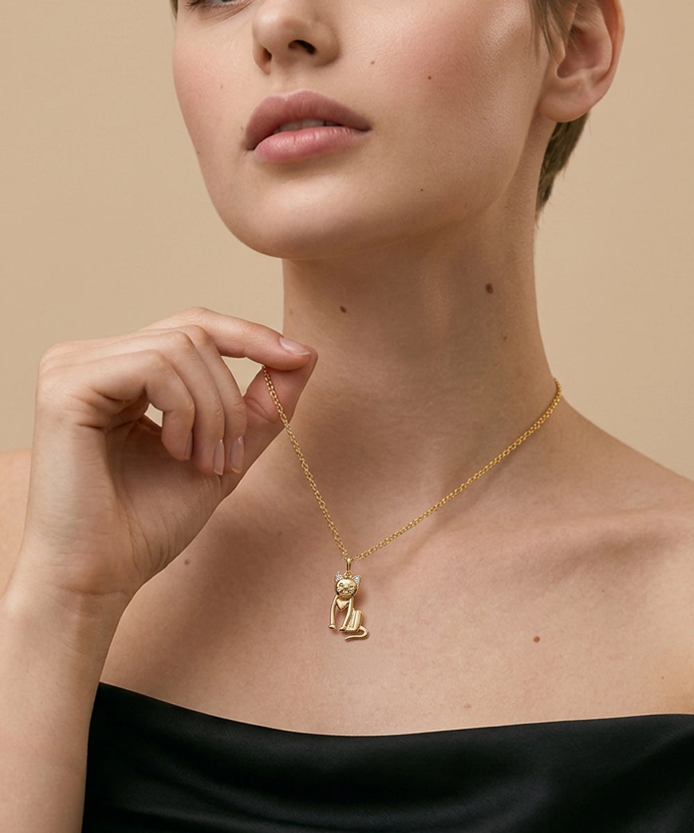 Woman wearing a gold necklace with a cat pendant against a beige background
