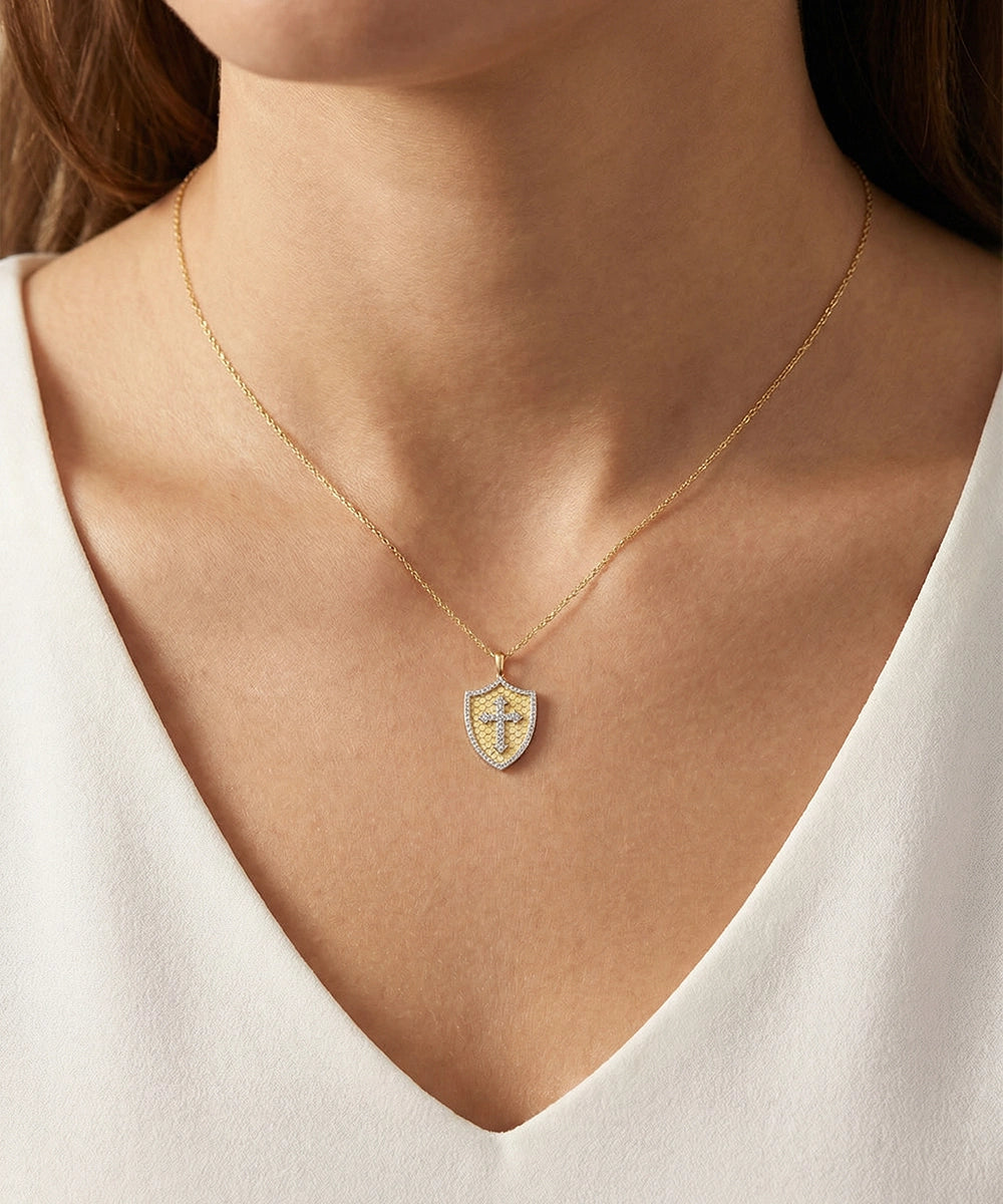 Gold necklace with a shield pendant worn by a person in a white top