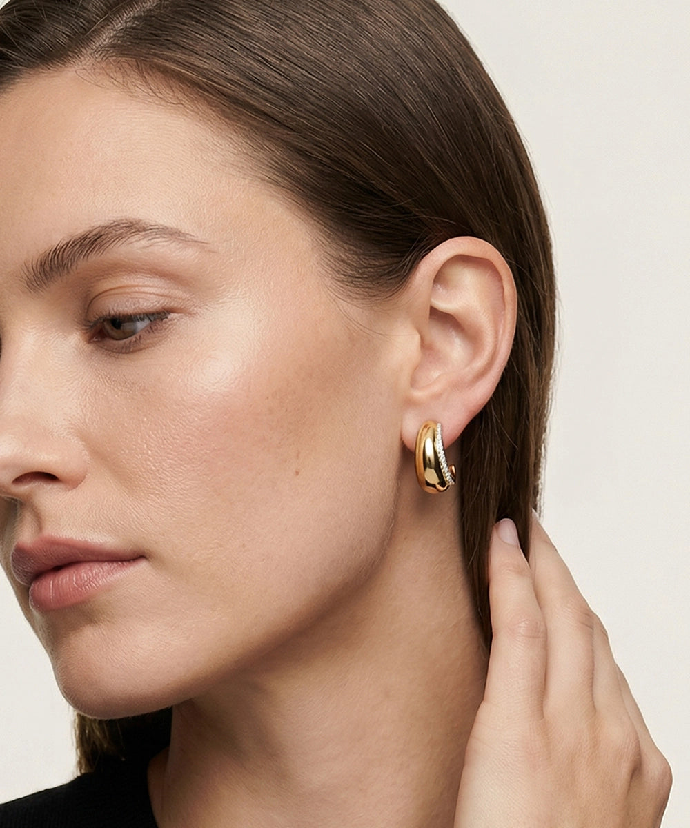 Close-up of a woman wearing gold hoop earrings with a neutral background