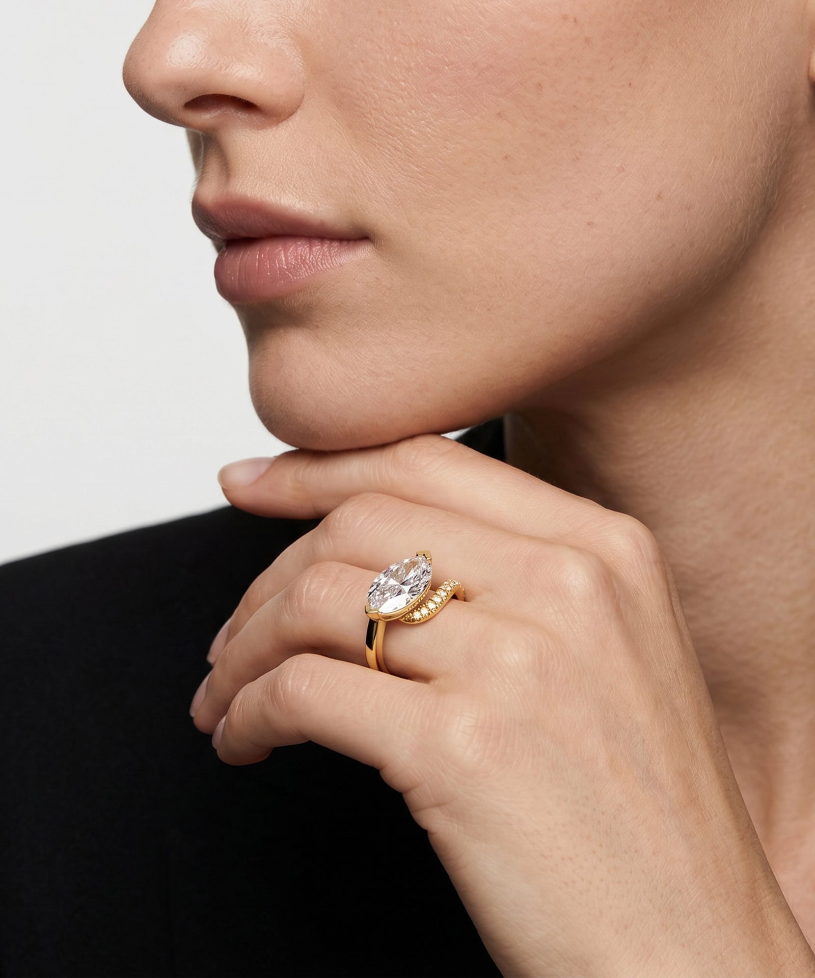 Close-up of a hand wearing a gold ring with a diamond on a neutral background