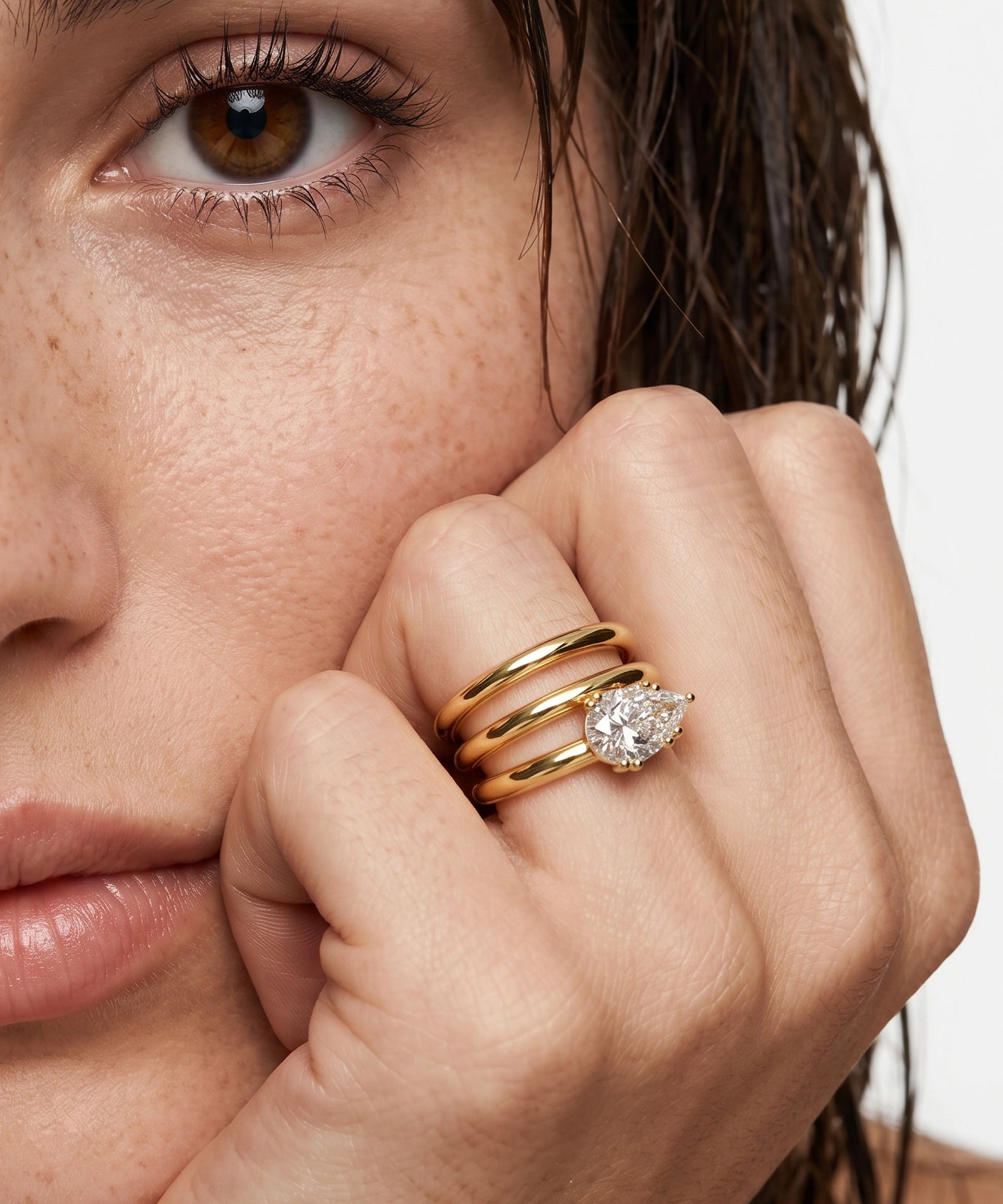 Close-up of a woman's face with a hand holding a diamond ring.