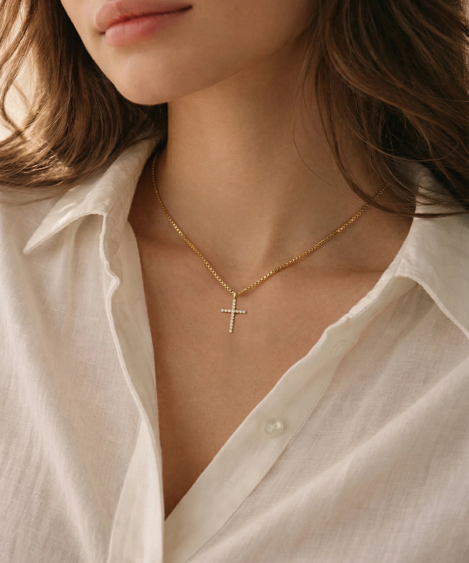 Gold necklace with a cross pendant worn by a person in a white shirt.