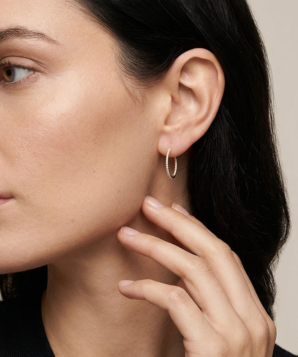 Close-up of a person wearing a gold hoop earring with a neutral background