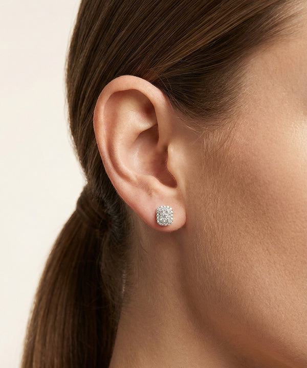 Close-up of an ear wearing diamond stud earrings with a neutral background