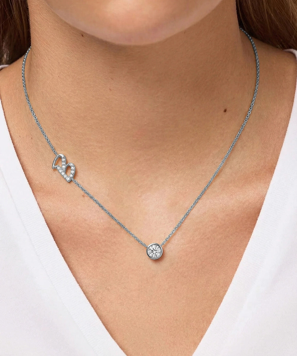 Silver necklace with heart and round pendant on a person wearing a white top.
