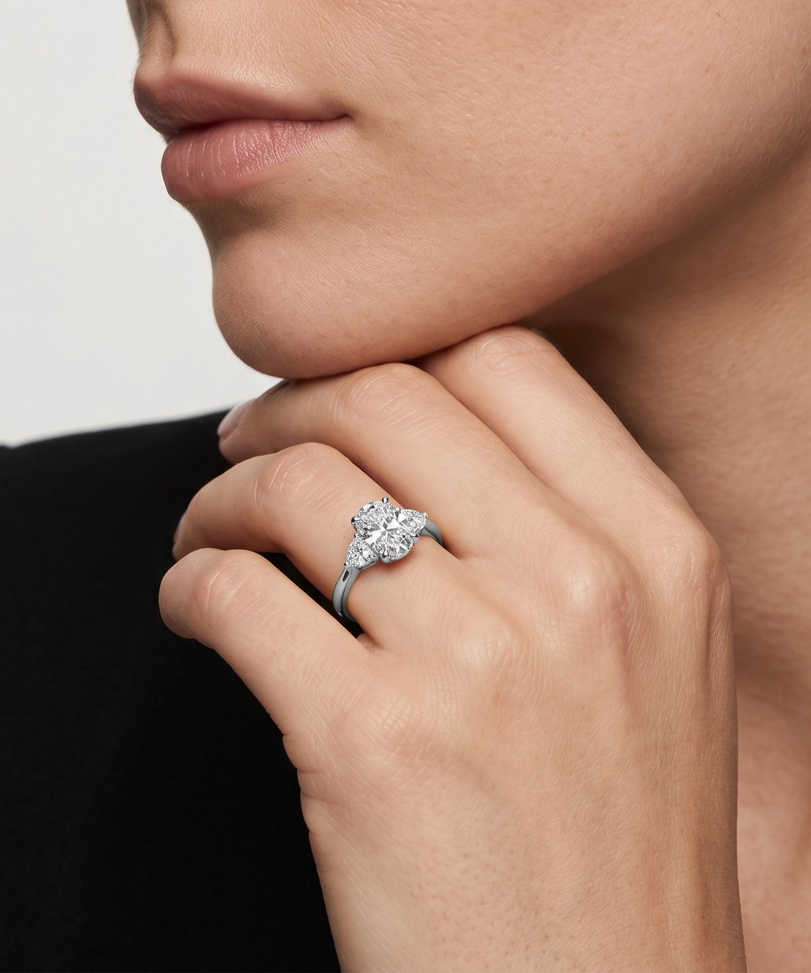 Three-stone oval diamond engagement ring shown on a model's hand.