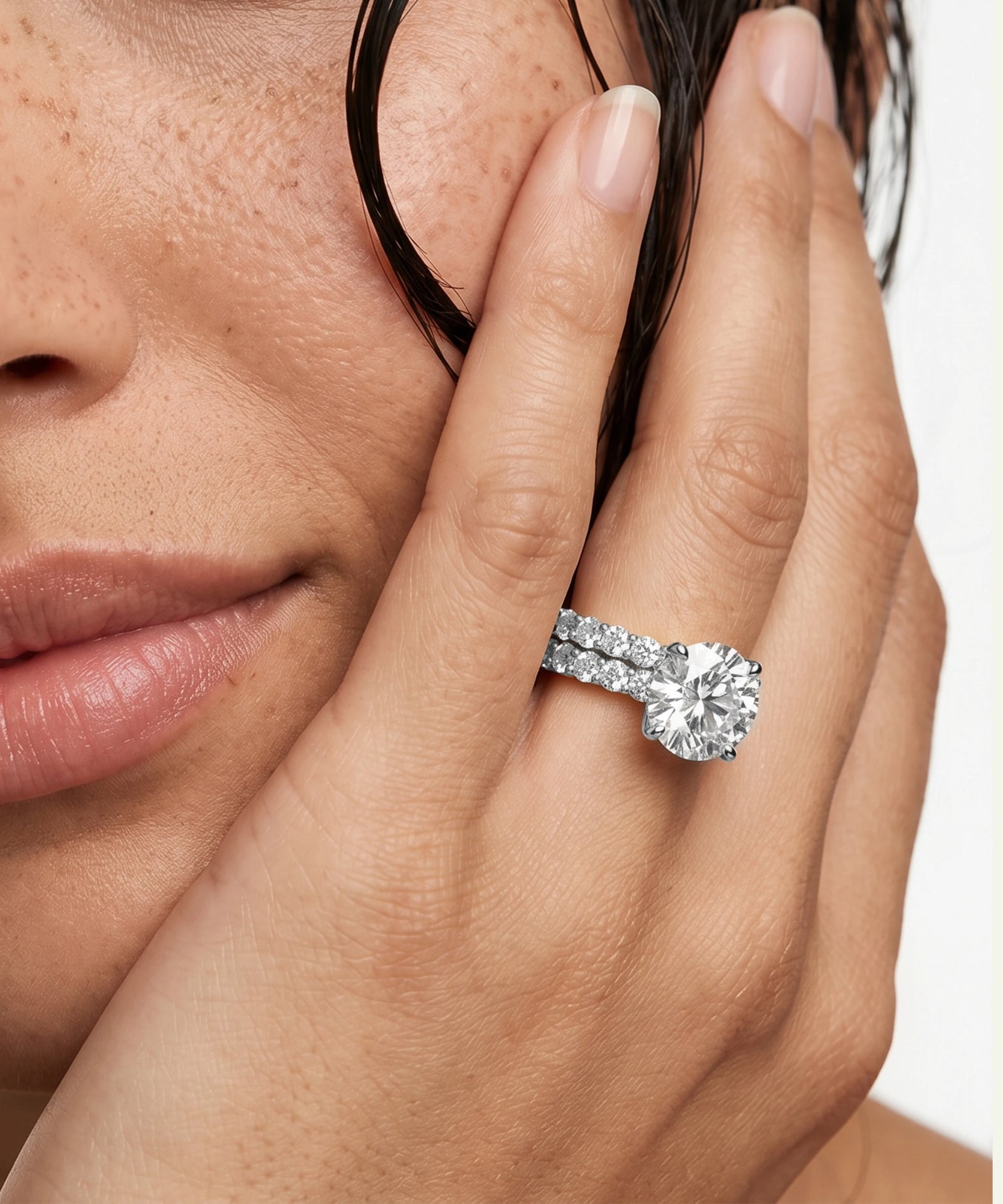 A close-up lifestyle shot of a model's hand wearing a yellow gold engagement ring with a round-cut diamond and a matching pavé band, set against a clean white background.