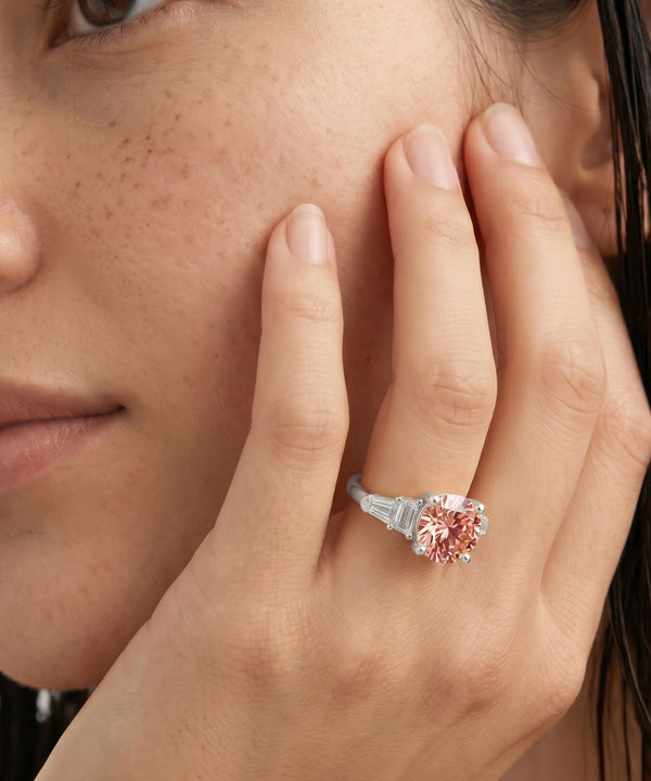 Close-up of a woman's hand wearing a pink gemstone ring, with a blurred background.