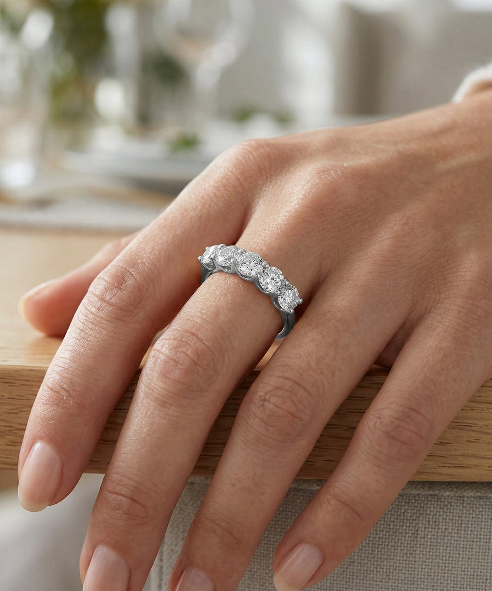Silver ring with diamonds on a person's finger against a blurred indoor background