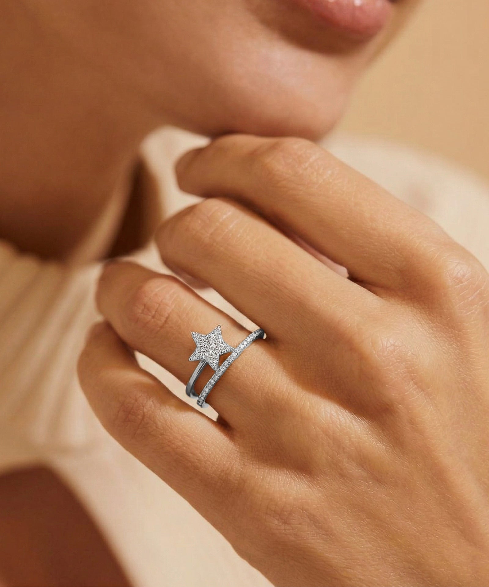 Close-up of a hand wearing a silver ring with a star design on a neutral background