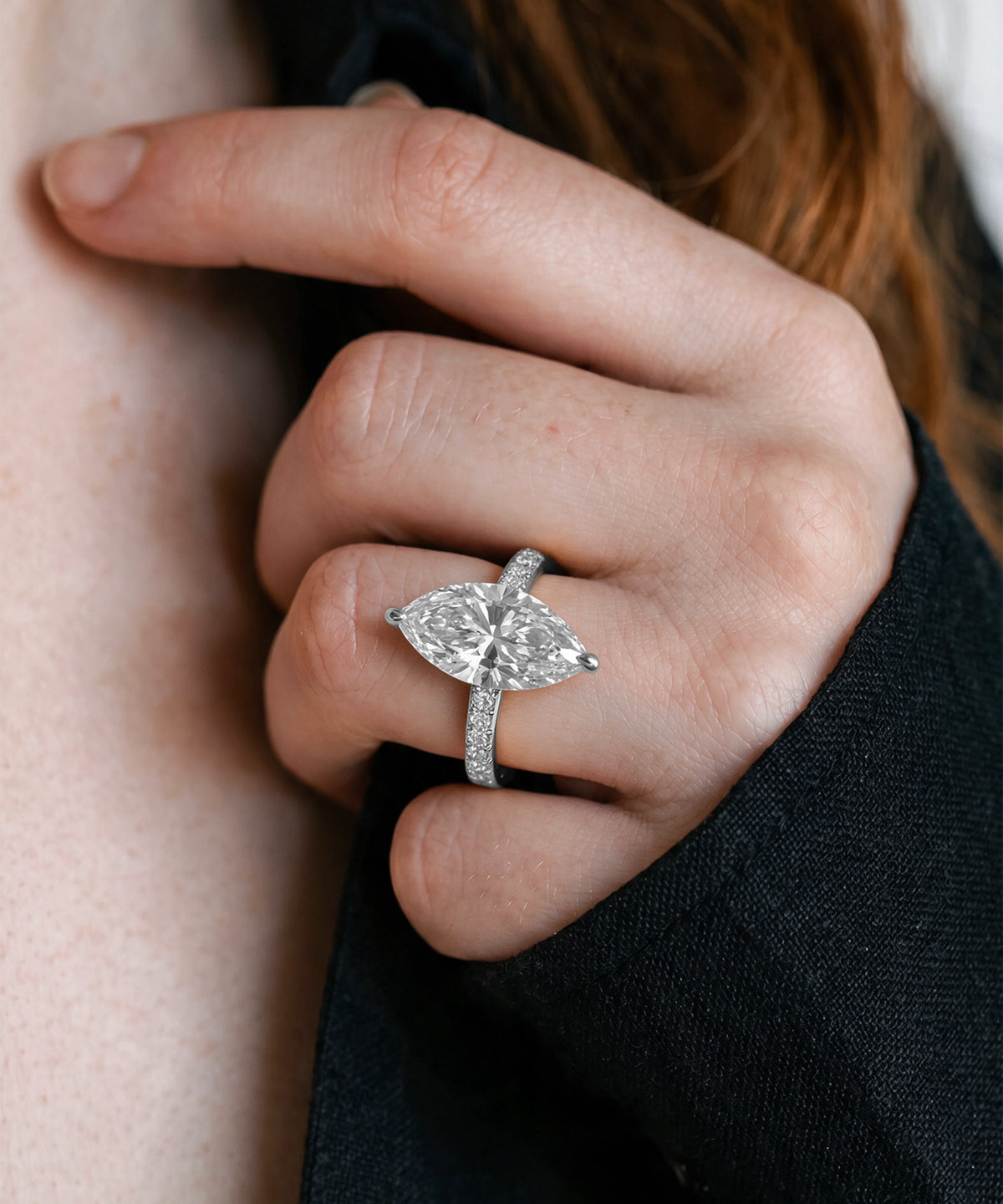 A close-up of a hand wearing a yellow gold ring with a large round diamond center stone and smaller diamonds along the band, set against skin and dark clothing.