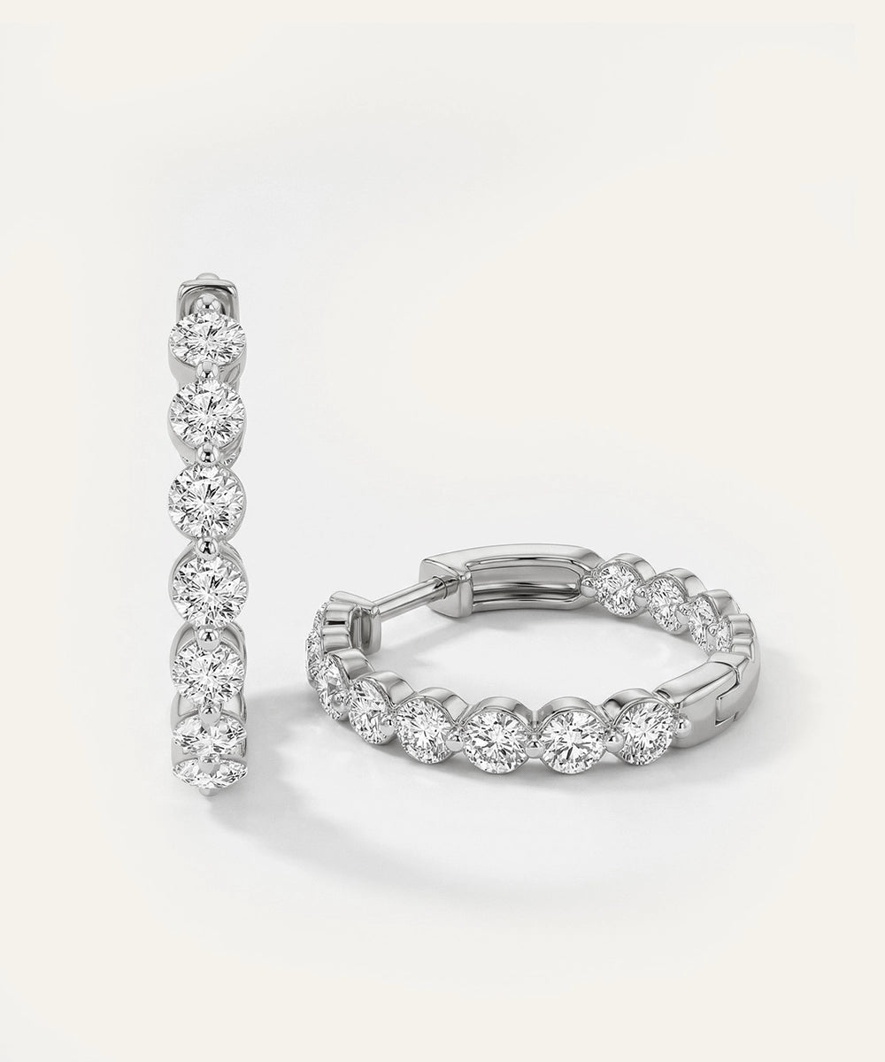 Pair of silver hoop earrings with clear gemstones on a light gray background
