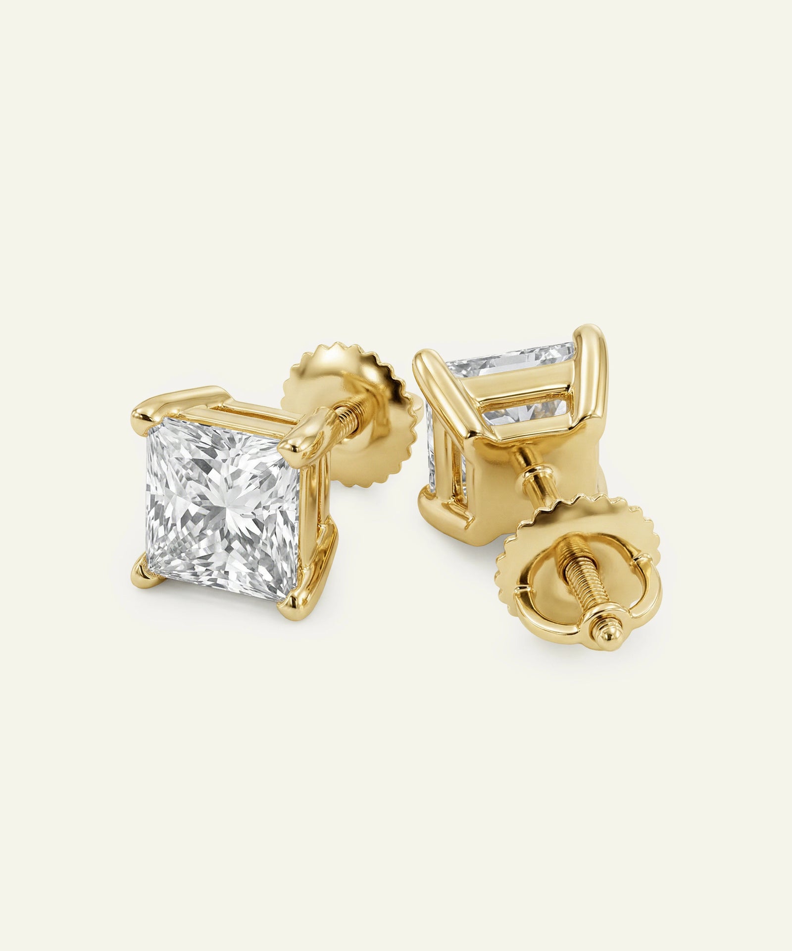 Gold stud earrings with clear gemstones on a light beige background