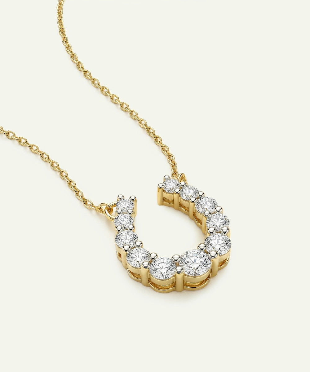 Gold necklace with a diamond-encrusted horseshoe pendant on a light gray background