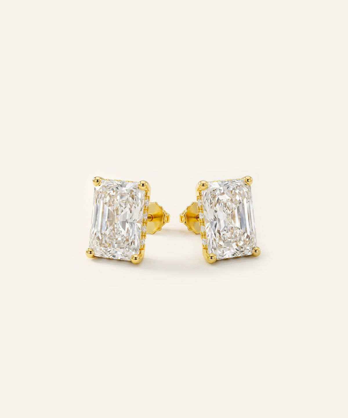 A pair of yellow gold stud earrings featuring rectangular emerald-cut diamonds, set against a clean off-white background.