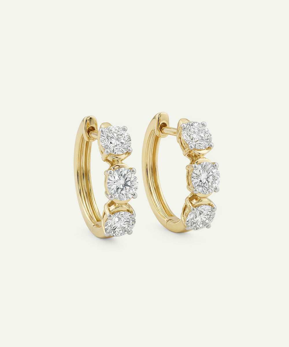 Gold hoop earrings with embedded diamonds on a light beige background
