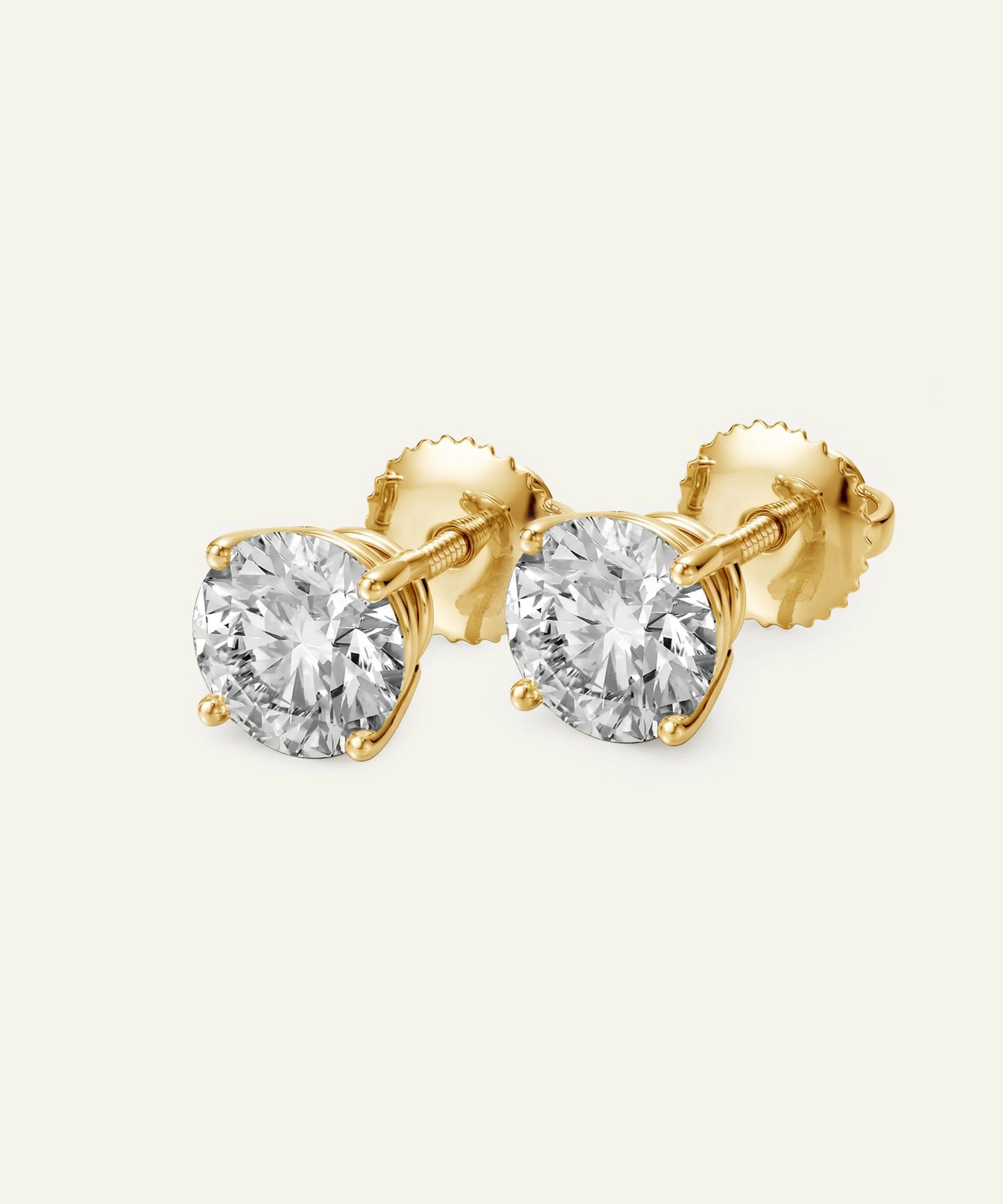 Gold stud earrings with clear gemstones on a light beige background