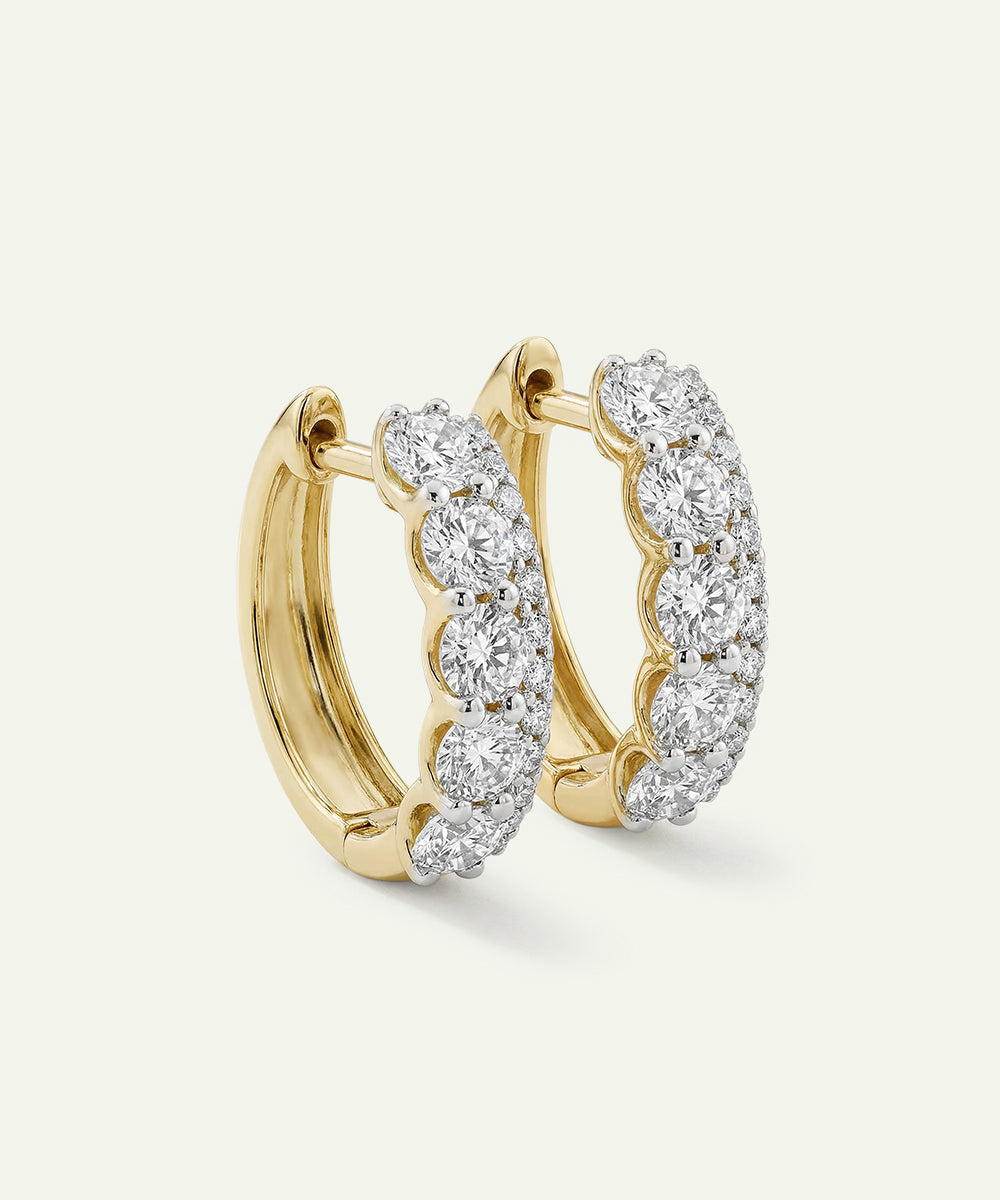 Gold hoop earrings with diamond accents on a light beige background