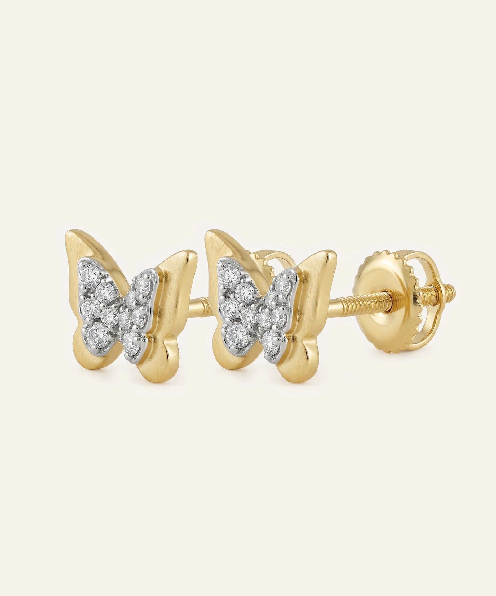 Gold butterfly earrings with diamond accents on a light beige background