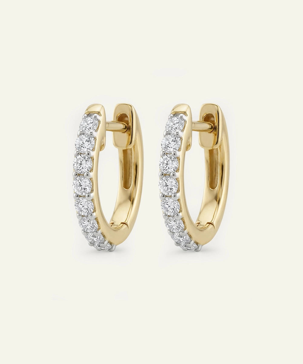 Gold hoop earrings with diamond accents on a light beige background