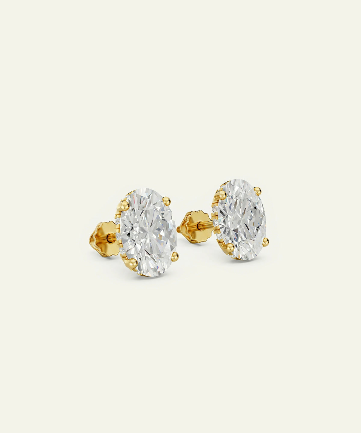 A pair of oval-cut diamond stud earrings in yellow gold settings, shown on a plain off-white background.