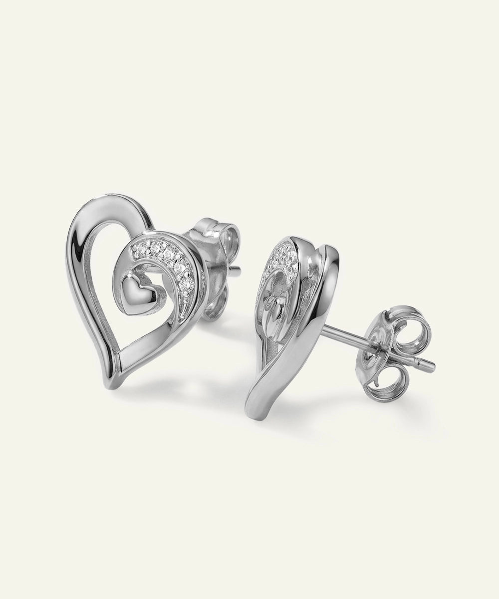 Heart-shaped silver earrings with clear gemstones on a light gray background