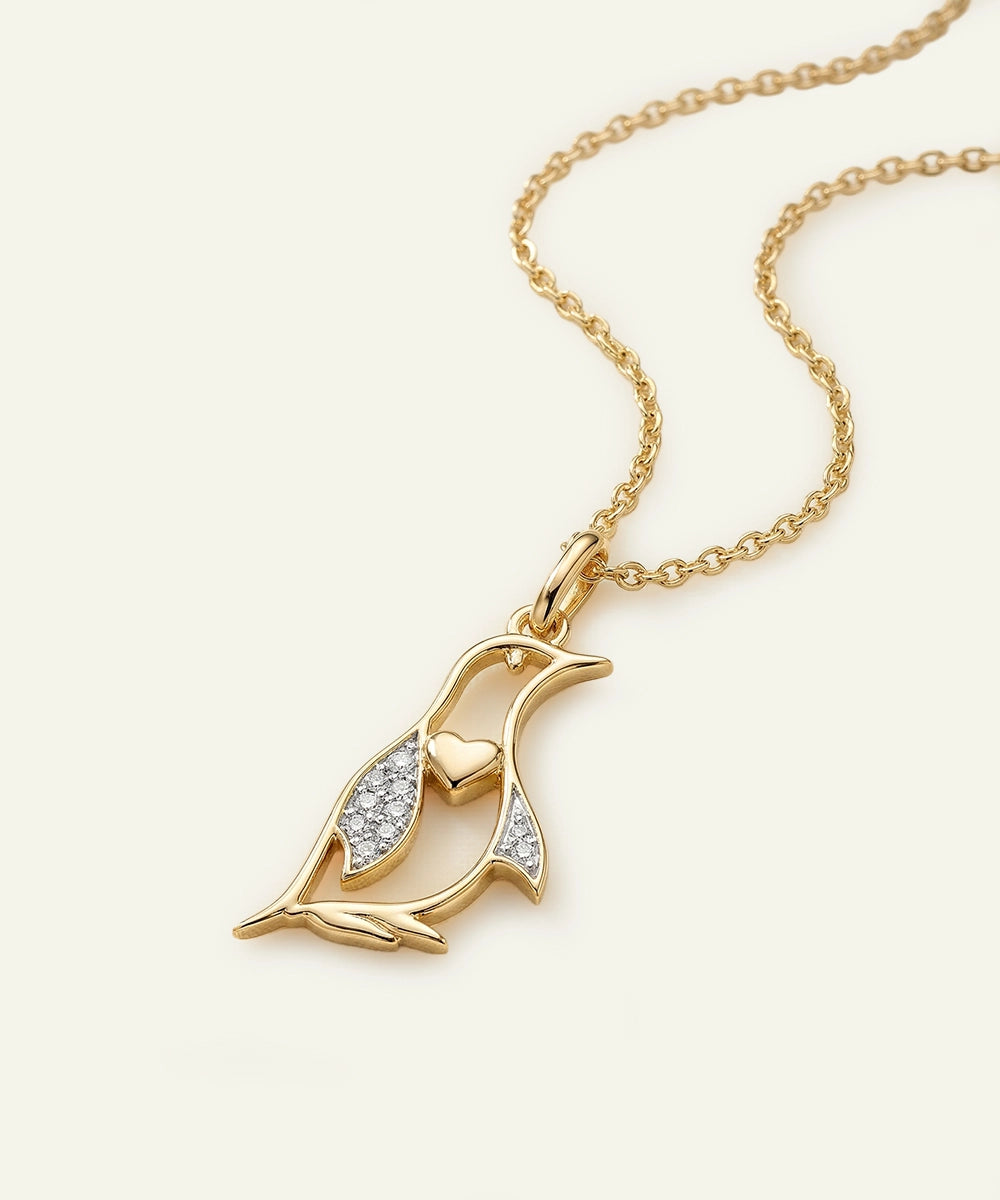 Gold necklace with a penguin-shaped pendant on a light beige background