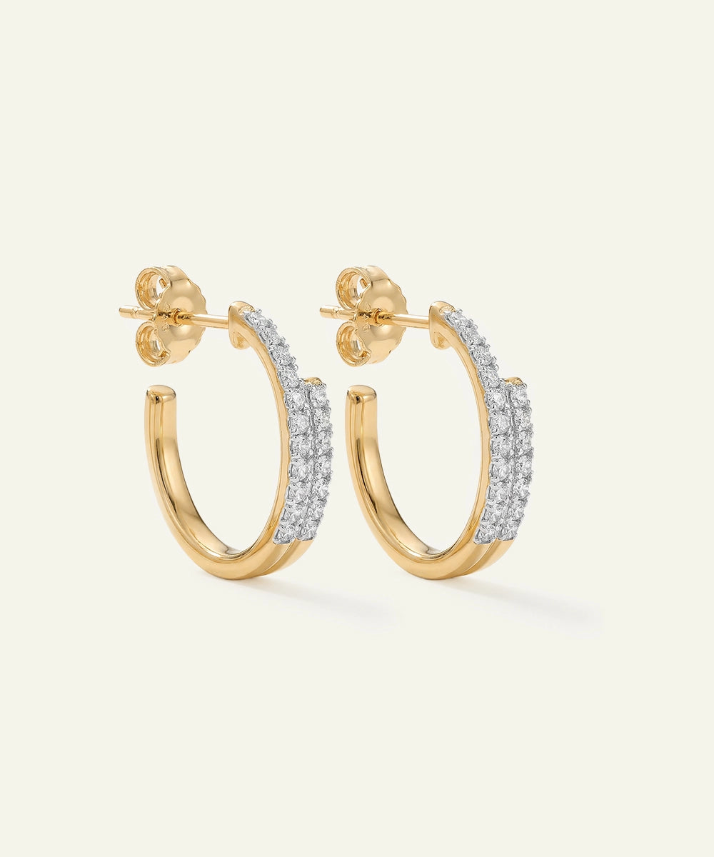 Gold hoop earrings with embedded diamonds on a light beige background