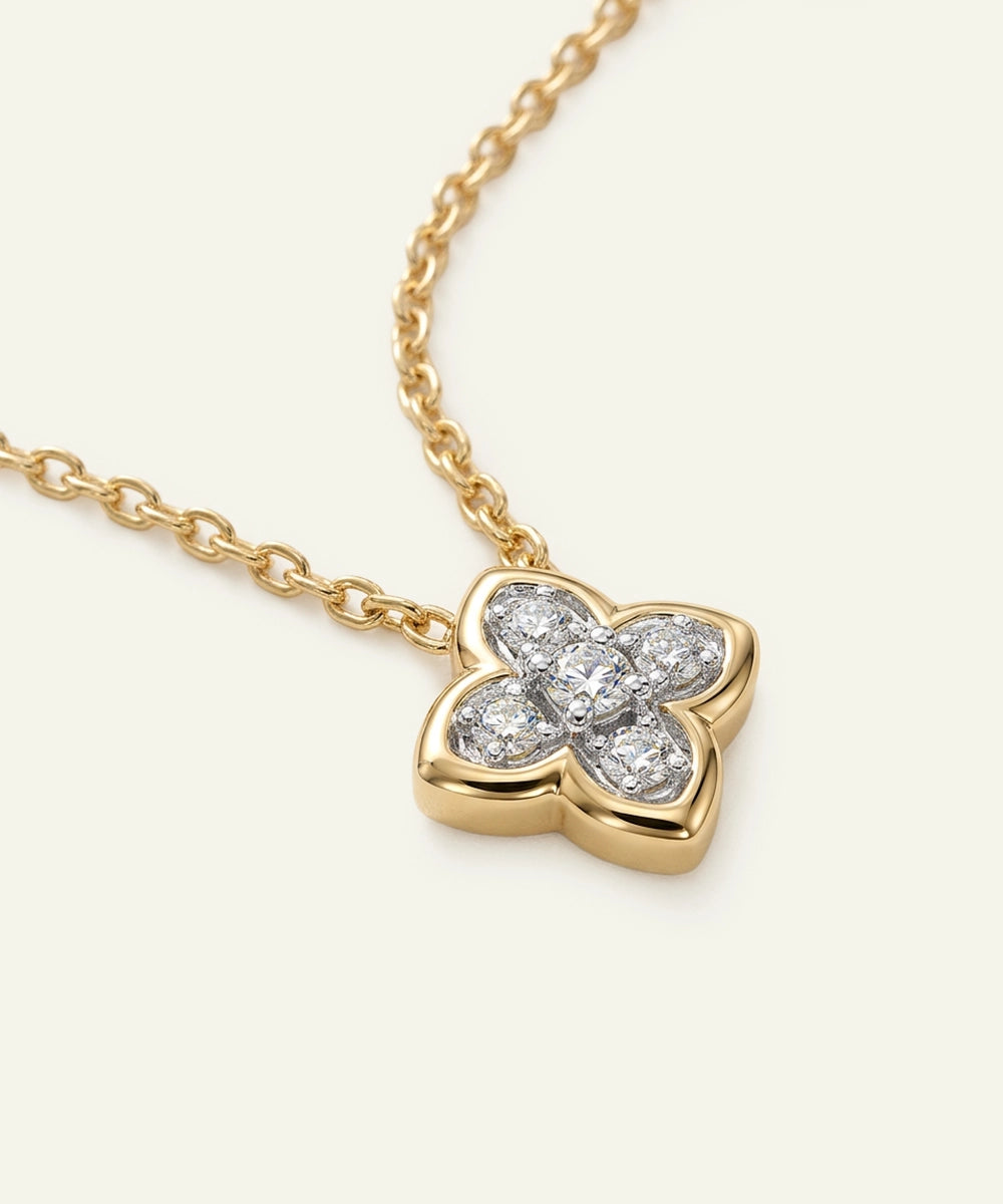 Gold necklace with a diamond-encrusted clover pendant on a light beige background