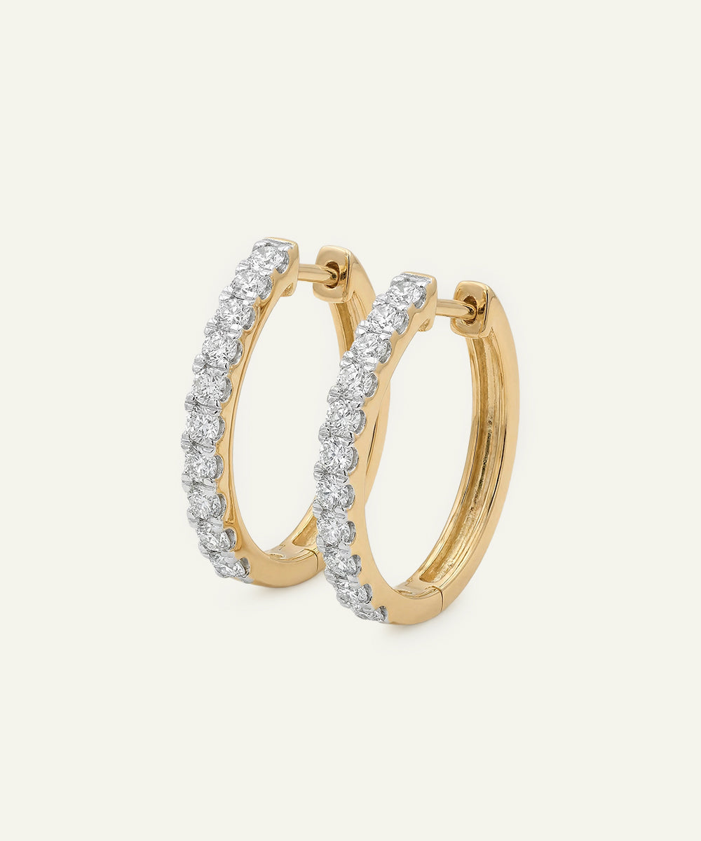Gold hoop earrings with diamond accents on a light beige background