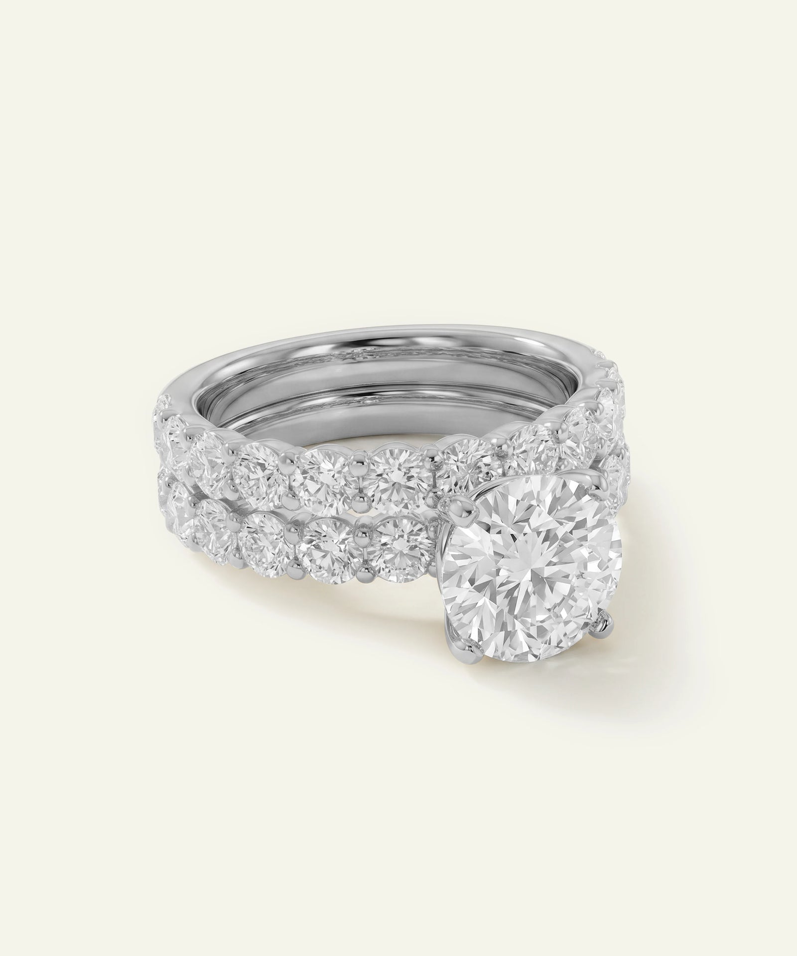 A double-row diamond ring set in silver-toned metal, featuring a large round-cut diamond solitaire and smaller diamonds along the band, shown on a light cream background.
