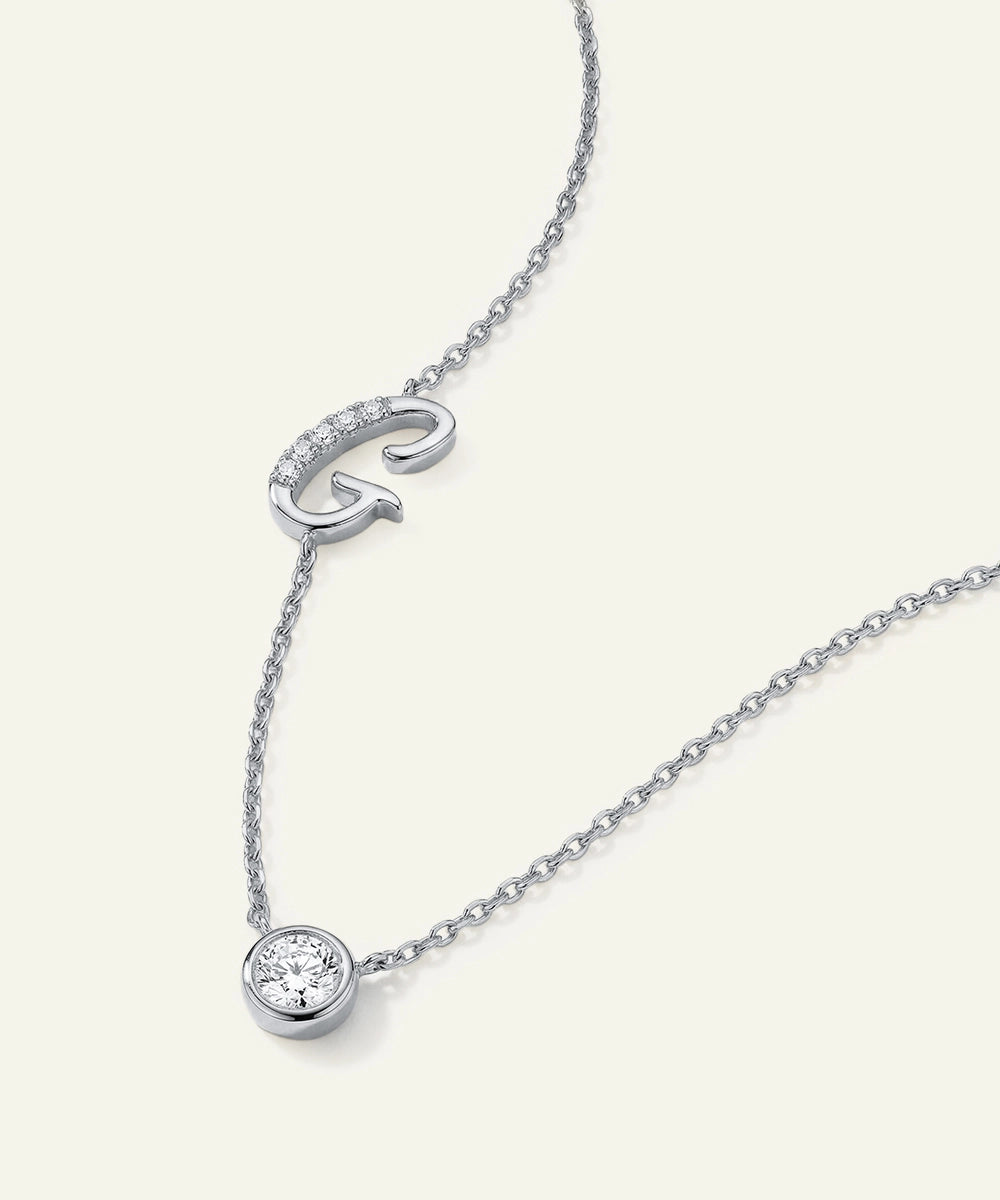 Silver necklace with a 'G' pendant and round diamond on a white background