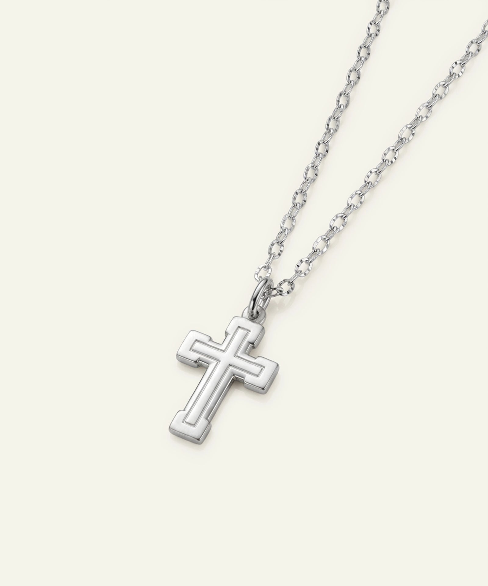 A silver cross pendant necklace with a matching chain, shown on a light cream background.