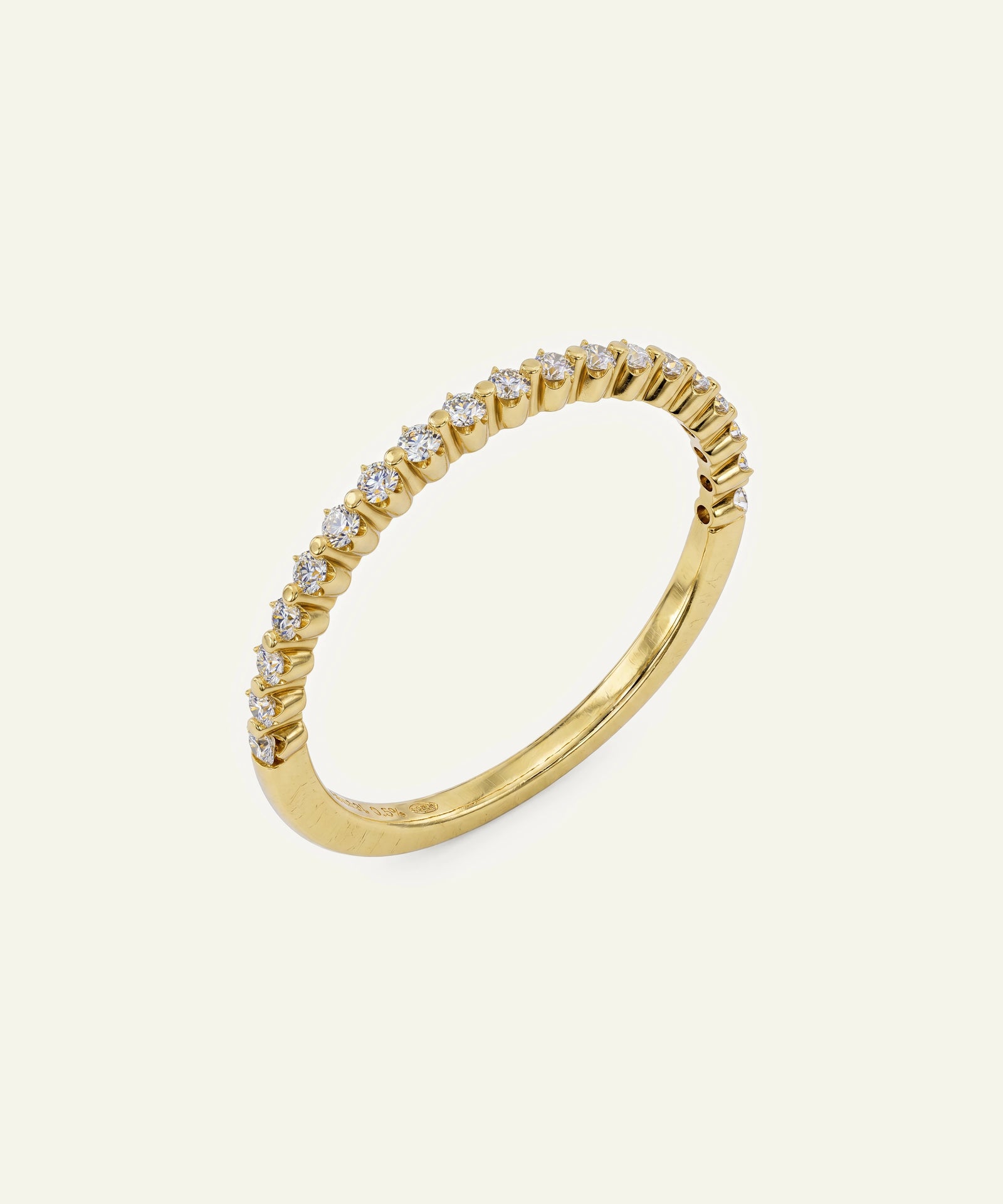 A gold ring featuring a curved row of small clear gemstones in a prong setting, photographed on a plain off-white background.