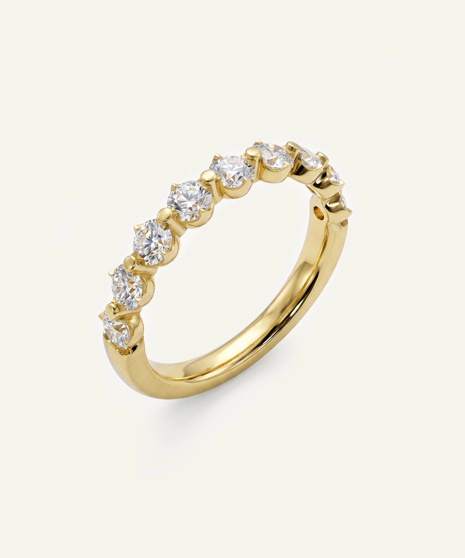 A yellow gold half eternity ring featuring a row of round brilliant-cut diamonds set in a half-prong setting, shown on a light cream background.