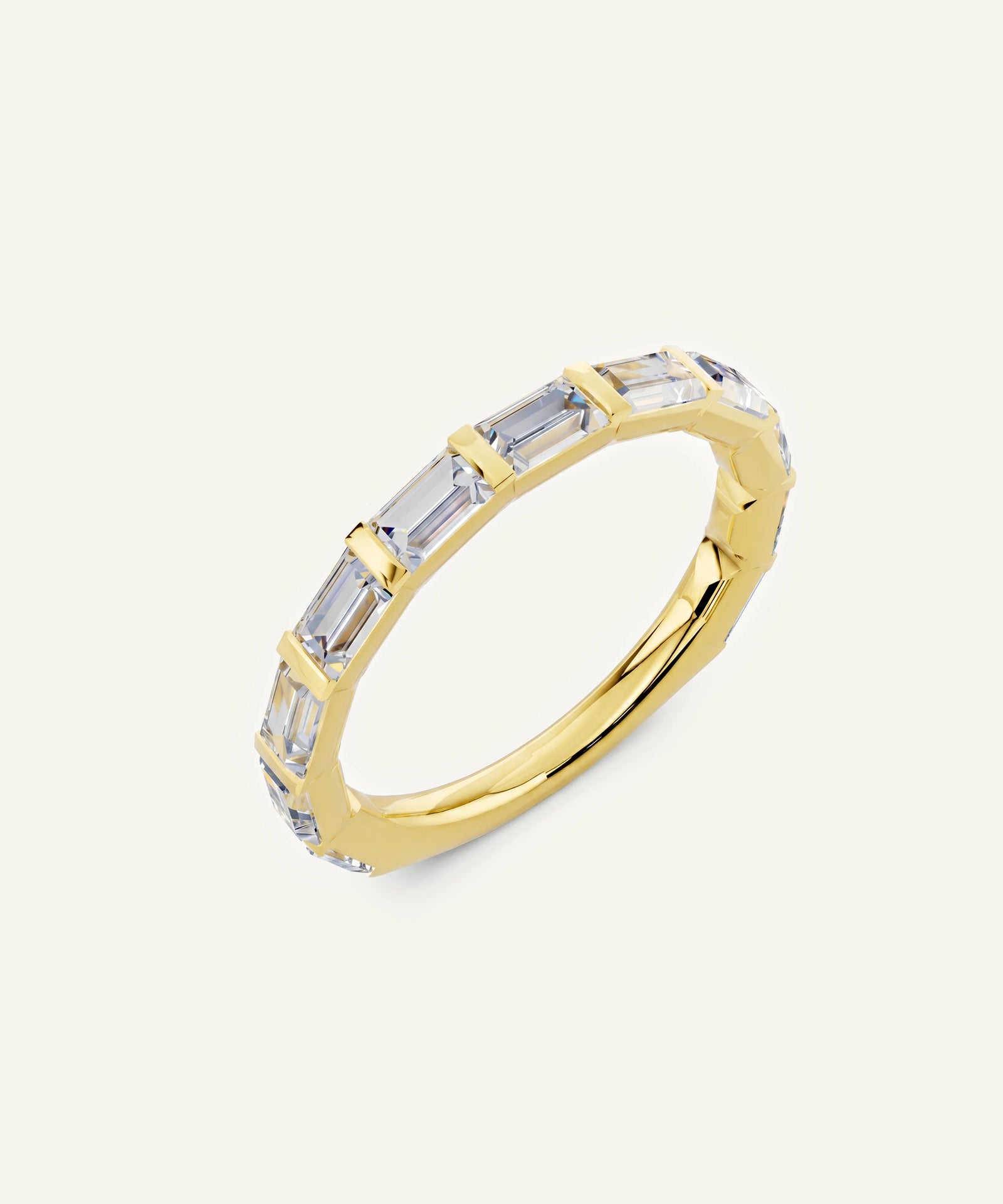 A gold band ring featuring a row of baguette-cut clear gemstones, shown on a light cream background.