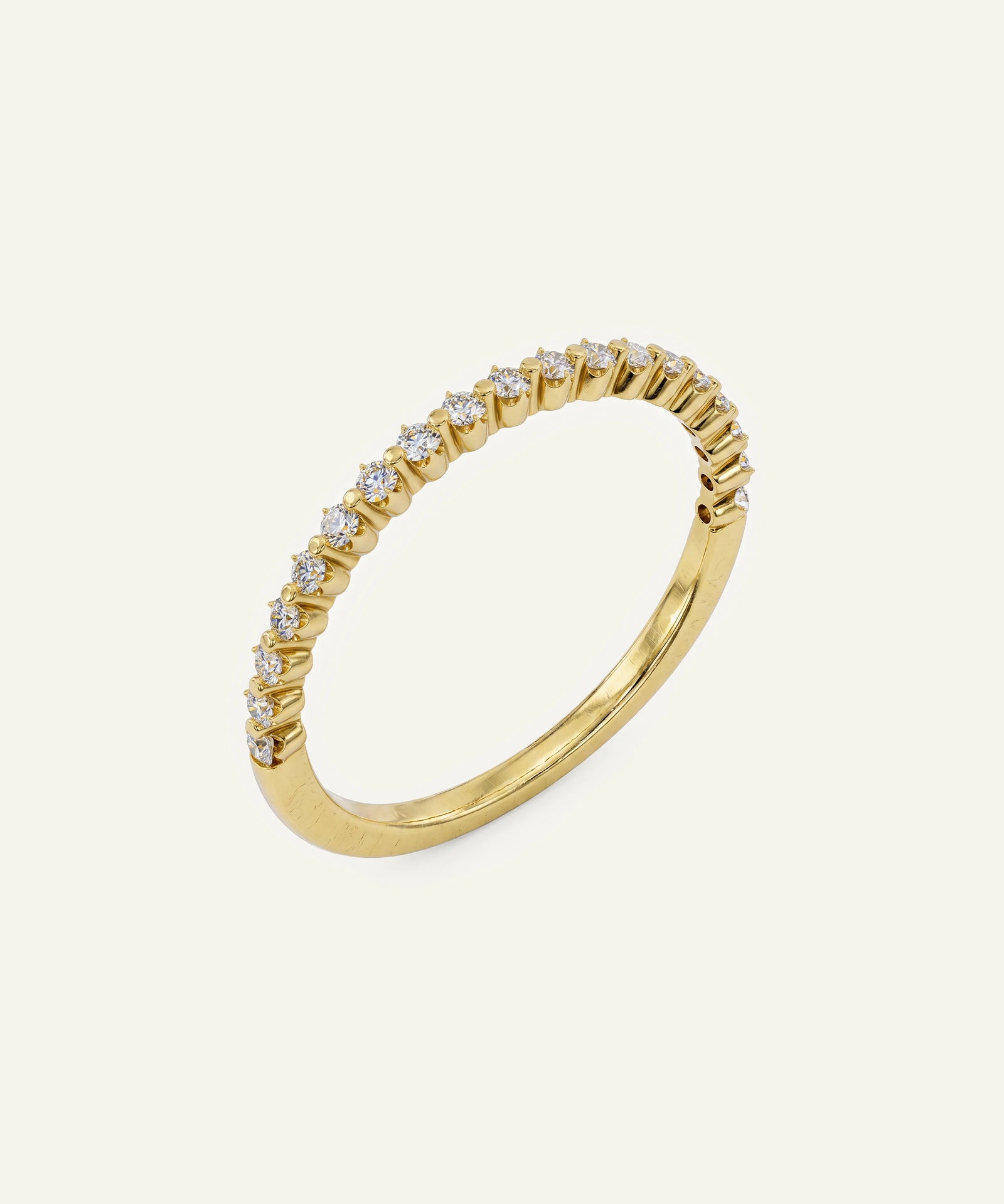 A gold ring featuring a curved row of small clear gemstones in a prong setting, photographed on a plain off-white background.