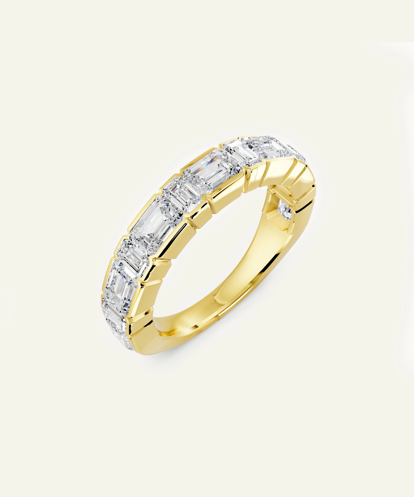 A yellow gold eternity ring featuring a continuous channel setting of baguette-cut clear stones, shown on a light cream background.