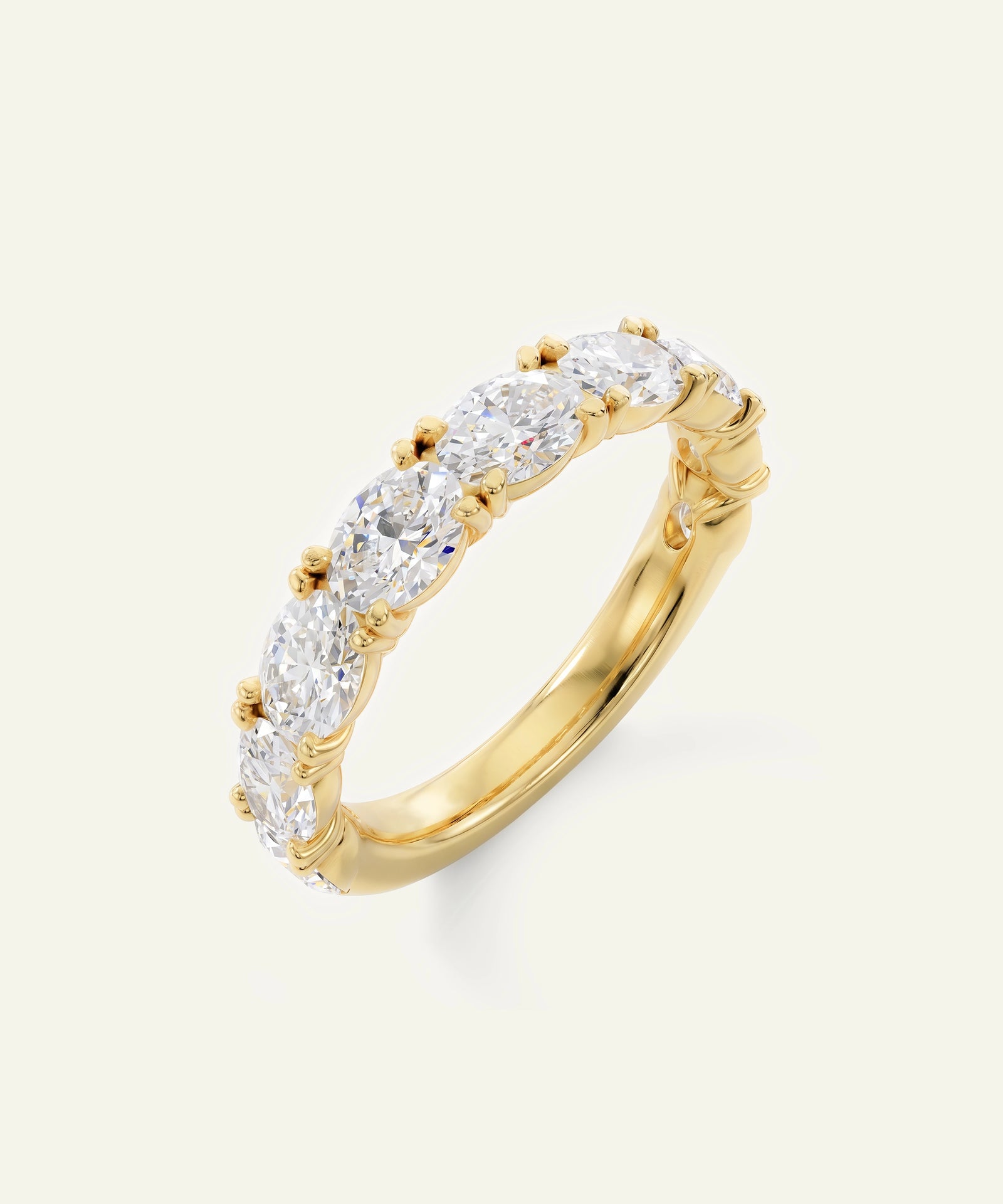 A yellow gold eternity-style ring featuring a row of round-cut clear gemstones in a prong setting, shown on a light cream background.