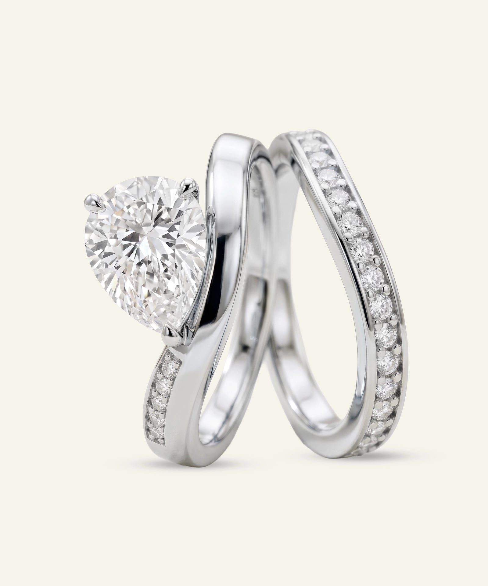 A silver-toned engagement ring with a round brilliant-cut diamond and a matching diamond-studded wedding band, displayed on a light cream background.